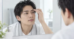 タオルを肩にかけ、鏡の前で眉周りを確認する男性のイメージ