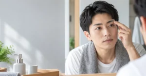 鏡の前で眉毛の状態を確認する男性の手元と顔のイメージ